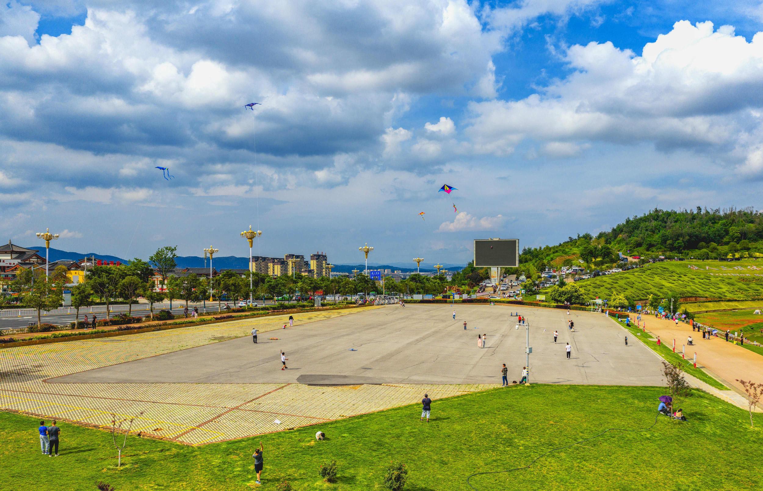 蓝天白云下，游客在广场上放风筝。